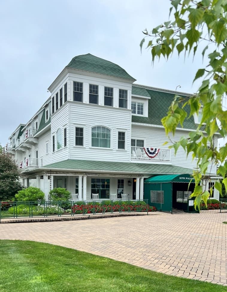 Exterior of Hotel Walloon with white siding, green roof, and covered entrance overlooking Village Green Park.